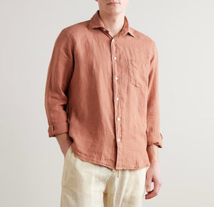 A man, seen from the back with hands in pockets, wears the HARTFORD - PAUL LINEN SHIRT IN FADED COPPER with rolled-up sleeves, paired with light pants.