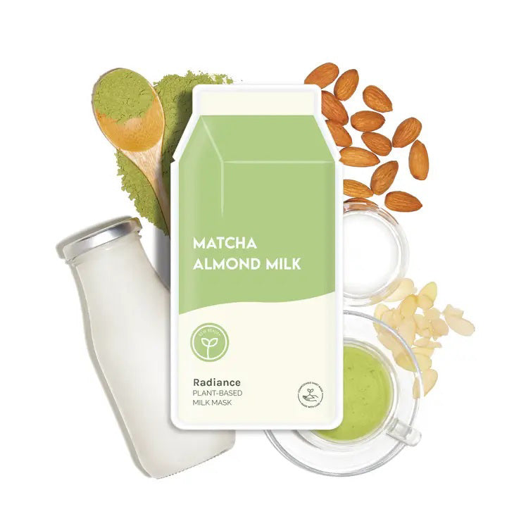 A carton labeled “ESW BEAUTY - MATCHA ALMOND MILK MASK” sits among milk, matcha powder, almonds, and a cup of green matcha—evoking the vegan matcha almond mask by ESW BEAUTY for a nourishing facial treatment.
