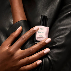A bottle of MANUCURIST INC GREEN™ Nail Polish in Gloss, featuring a vegan, cruelty-free formula in a pale pink shade with a black cap. The label reads “green, quick dry intense color, nail polish gloss.”.