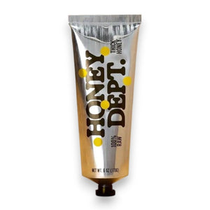 A metallic tube labeled “HONEY DEPARTMENT- THICK HONEY TUBE” stands upright against a brown gradient background. The design features yellow dots and bold black text, resembling a toothpaste or paint tube—making it perfect for dispensing thick honey with ease from HONEY DEPARTMENT.