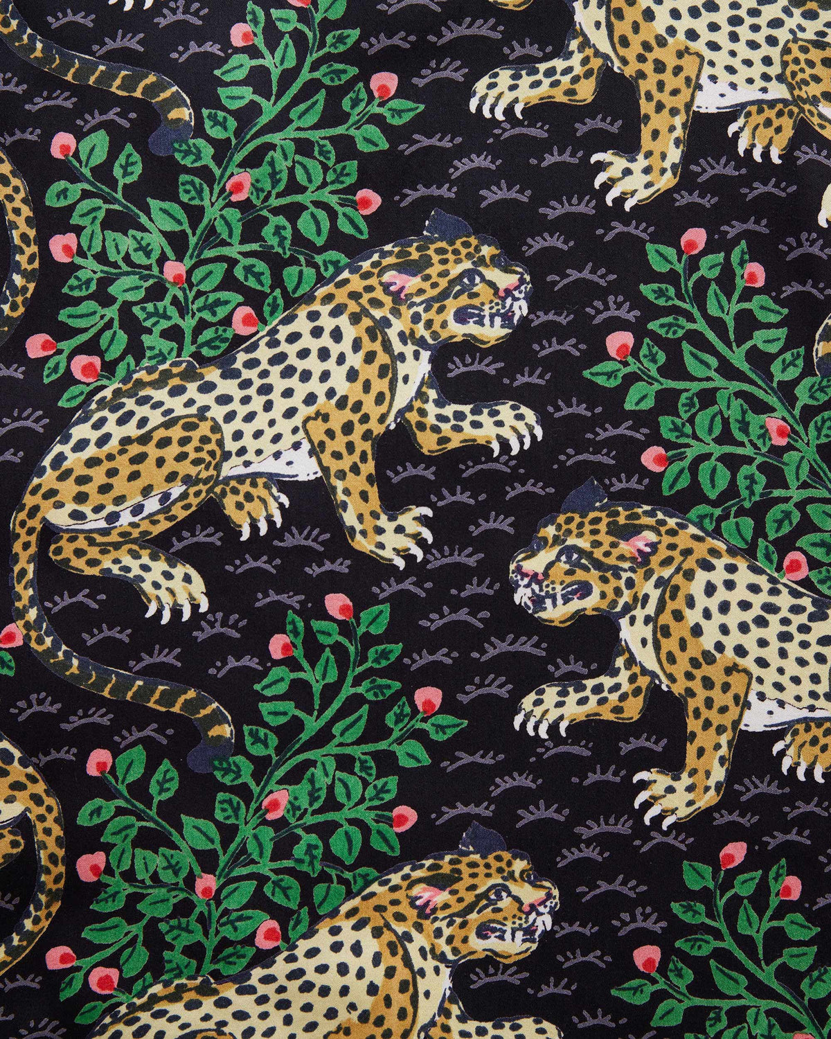A woman stands barefoot on a woven rug in front of a white paneled wall, wearing the PRINTFRESH - Bagheera Satin Wildest Dream Pajama Set in Ink from PRINTFRESH, featuring a vibrant leopard and foliage pattern with wide-leg pants.