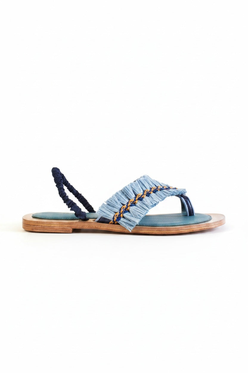 The MEHER KAKALIA - HAMAM SLIDE IN SONIC SAPHIRE by MEHER KAKALIA features a flat wooden sole, teal footbed, blue frayed-edge fabric straps, and yellow and navy textured raffia detail across the top.