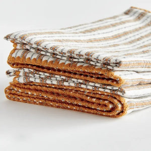 Elevate your table linens collection with the NAPA HOME AND GARDEN - SUTTON DINNER NAPKIN. This folded cotton napkin, featuring brown, white, and gray vertical stripes accented by decorative brown stitching along the edges, offers a stylish soft ochre touch—perfect for bringing both elegance and versatility to any dining setting. Displayed against a crisp white background, it’s a standout piece from NAPA HOME AND GARDEN.
