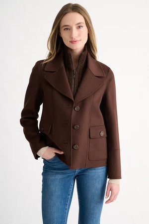 A close-up shows a person wearing the KINROSS Knit Insert Notch Collar Coat in Chocolate, featuring a wide lapel and crafted from luxurious wool cashmere, layered over a dark brown high-neck zip-up sweater. Only the neck, shoulder, and part of the face are visible.