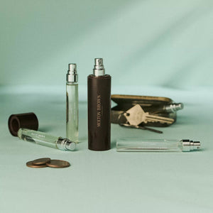 A dark brown cylindrical MOLTON BROWN 7.5ML Eau de Parfum bottle sits inside a matching rectangular MOLTON BROWN Travel Case with a white interior, both displayed against a plain white background.