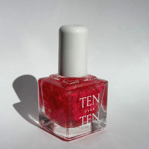 A glass bottle of TENOVERTEN - NAIL POLISH from the brand TEN OVER TEN, featuring a white cap and a dusty pink nail color. The front label displays "TEN OVER TEN" in white uppercase letters. This vegan, eight-free formula ensures both beauty and peace of mind. The background is plain and light-colored.