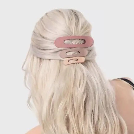 A pink card presents the KITSCH - FLAT LAY CLAW CLIP 3 PCS, featuring three clips in gradient shades of pink and mauve, from light to dark. Adorned with a logo and text, it emphasizes their crafting from recycled plastic.