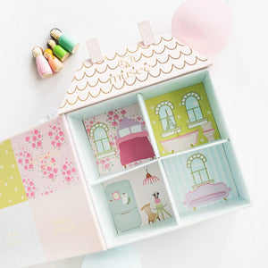 The MUSEE - DOLLHOUSE BATH BALM SET by MUSEE features a pastel, house-shaped gift box reminiscent of a dollhouse, complete with whimsical labeling. Inside, four naturally crafted bath balms—Fresh Linen, Flowering Lilies, Clean Citrus, and Warm Vanilla—are nestled in white decorative paper. This delightful set makes for a charming children’s gift.