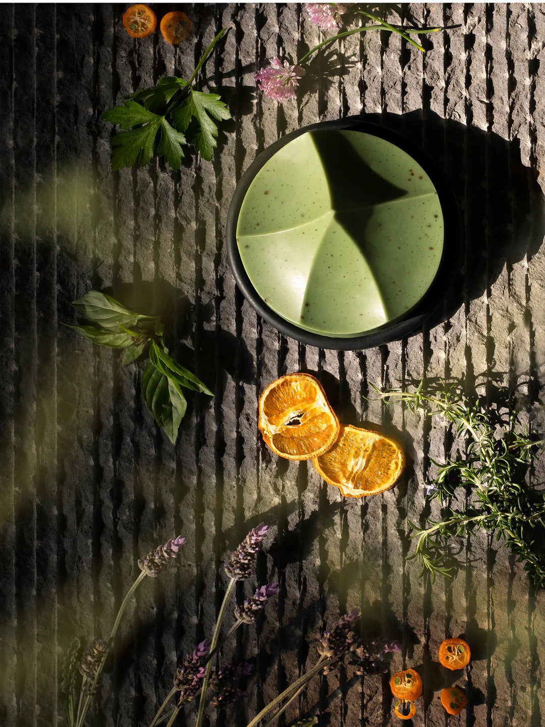 The UME – HERBES DE PROVENCE ERODE SOAP by UME STUDIO is a sculptural, geometric light green bar with subtle speckles and three peaked curves, displayed on a round dark soap dish against a plain white background.