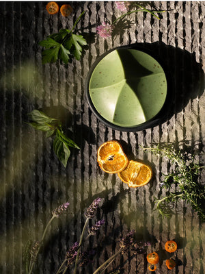 The UME – HERBES DE PROVENCE ERODE SOAP by UME STUDIO is a sculptural, geometric light green bar with subtle speckles and three peaked curves, displayed on a round dark soap dish against a plain white background.