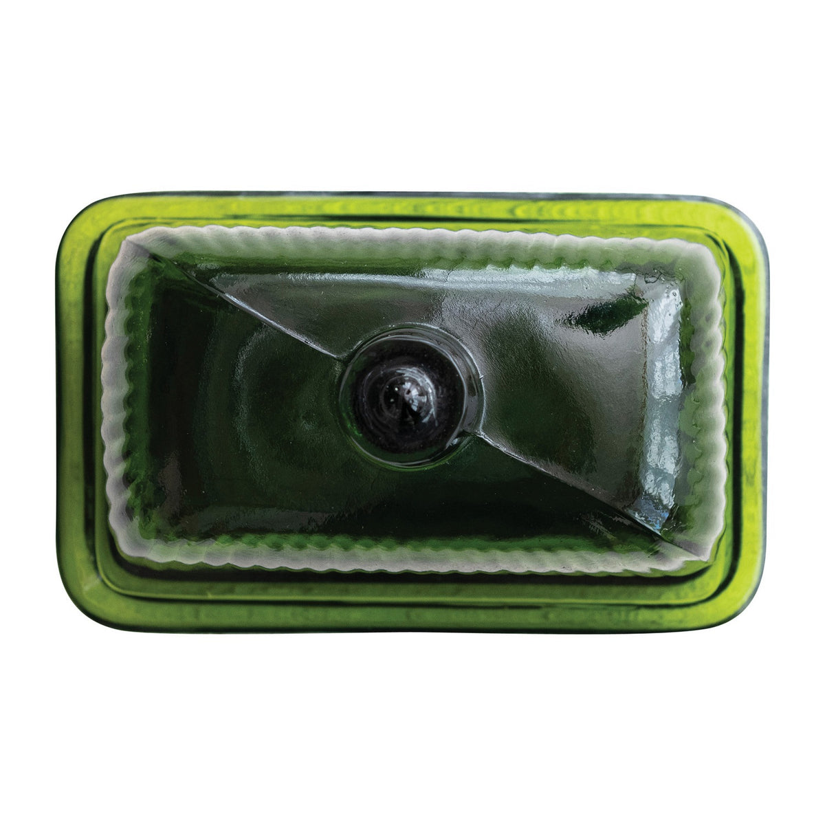 The CREATIVE COOP GREEN PRESSED GLASS BUTTER DISH is displayed with green glass containers and bottles on a textured white surface, beside a folded towel and a partially visible book.