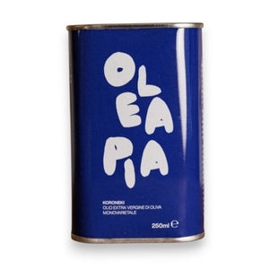 A 250ml blue tin labeled “OLEA PIA” in bold white letters contains OLEA PIA - MONOVARIETAL KORONEIKI EXTRA VIRGIN OLIVE OIL, a premium Greek olive oil that is cold-pressed to retain its exceptional flavor and aroma.