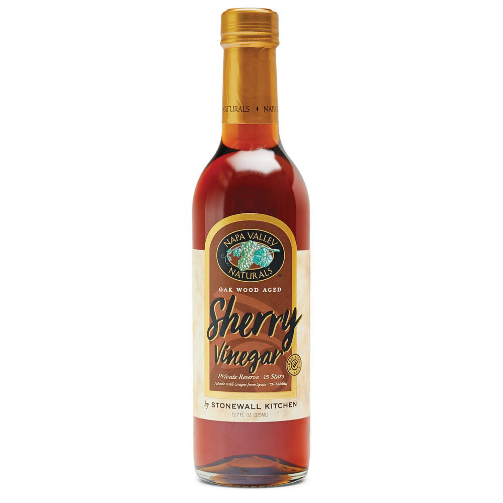 A bottle of Stonewall Kitchen Sherry Vinegar. The transparent bottle with a golden cap holds amber-colored aged sherry vinegar. Its beige label features black and red text, complemented by a green vineyard illustration, highlighting its Spanish Palomino grapes origin.