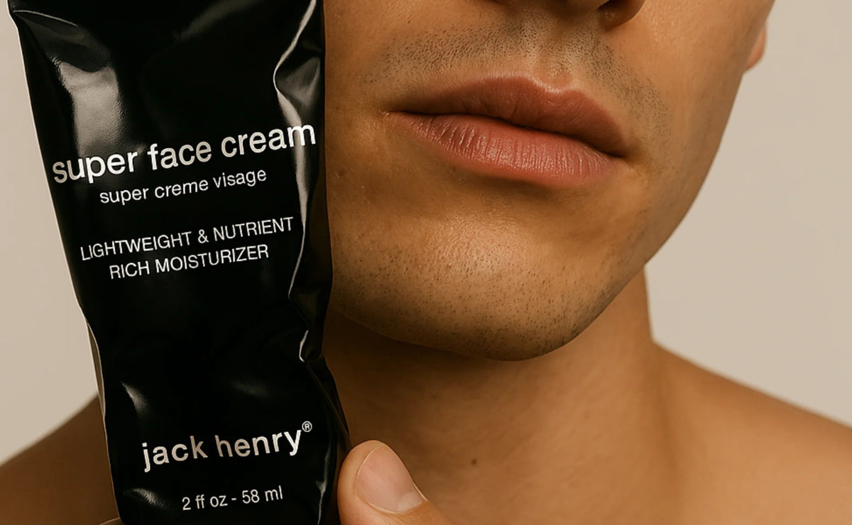 A black tube of JACK HENRY - SUPER FACE CREAM, branded with "JACK HENRY" in white text and topped with a black cap, rests on a white background casting a right-side shadow—a minimalist moisturizer ideal for anti-aging skincare.