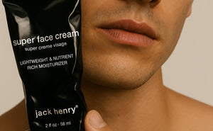 A black tube of JACK HENRY - SUPER FACE CREAM, branded with "JACK HENRY" in white text and topped with a black cap, rests on a white background casting a right-side shadow—a minimalist moisturizer ideal for anti-aging skincare.