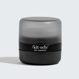 A small, round black container with a matte gray cap labeled "KITSCH Volumizing Rice Protein Dry Shampoo - Dark Tinted" rests on a light gray background—ideal for absorbing oil and refreshing dark hair.