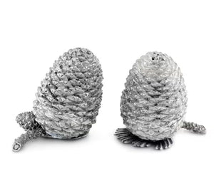 Two detailed silver pine cones stand upright on a white background, resembling the VAGABOND HOUSE - PEWTER PINE CONESALT AND PEPPER SET by VAGABOND HOUSE, with small pine needle segments visible at their bases.