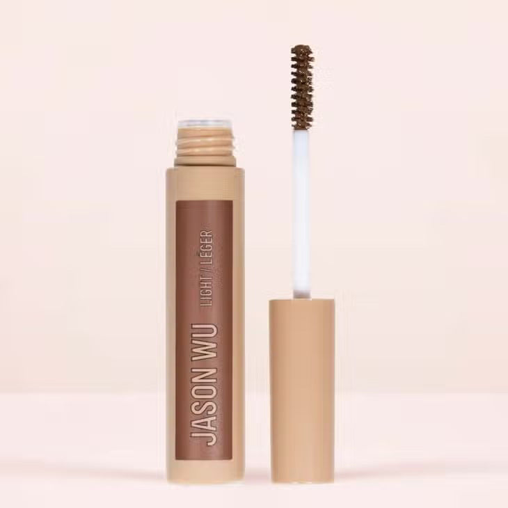 A cylindrical makeup product labeled &quot;FREE DA BROW LIGHT 2&quot; by JASON WU BEAUTY in white text against a beige background. The container features a matte finish and a beige cap, designed to help you define your brows effortlessly. Set against a neutral, light-colored background, the image captures its sleek elegance.