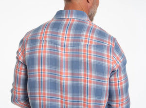 Close-up of a person's chest in the CRIQUET - DOUBLE CLOTH FLANNEL PEARL SNAP SHIRT IN SUNSET, a blue, white, and orange plaid flannel with pearl snaps, front pocket with flap, and visible chest hair at the open collar.