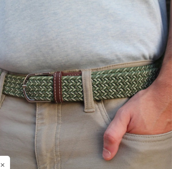 The ROOSTAS - REMINGTON WOVEN STRETCH BELT features a green herringbone weave, brown leather accents with embossed logo, decorative stitching, and a silver buckle. Adjustable for comfort and style on any occasion.