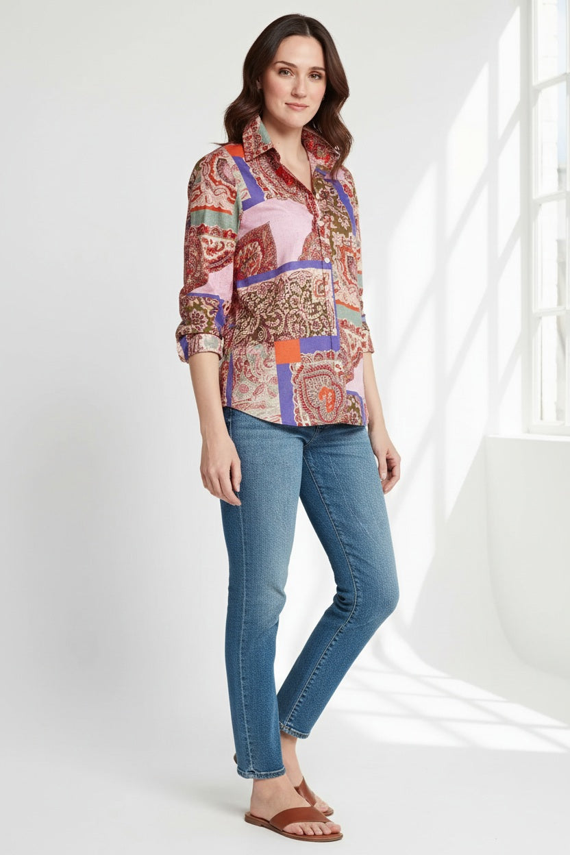 A woman stands against a plain background wearing the HINSON WU - REESE LONG SLEEVE SHIRT, a relaxed fit patchwork paisley top in pink, red, purple, and green, paired with blue jeans. She looks confidently at the camera with one hand in her pocket.