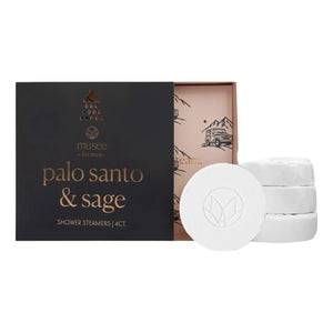 A box labeled “MUSEE - PALO SANTO & SAGE SHOWER STEAMERS” by MUSEE sits next to four white, round steamers featuring an elegant leaf design. The sleek black box with gold lettering is slightly open to reveal its illustrated inner packaging. This specialty MUSEE sage shower steamer elevates your daily routine, turning each shower into a luxurious aromatherapy experience.