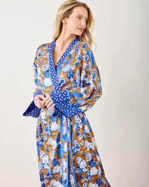 A person stands barefoot on a wooden floor, wearing the eco-friendly PRINTFRESH Satin Fancy Cat Robe with a blend of blue, white, and brown patterns. They pose with one hand on their chin and a neutral expression against a plain light-colored background.