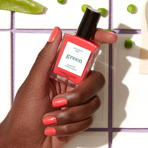 A bottle of MANUCURIST INC’s GREEN™ Nail Polish in the shade “Pulp,” showcasing a vibrant coral hue, with a sleek black cap and a label that reads “green quick dry intense color,” made using bio-sourced ingredients.