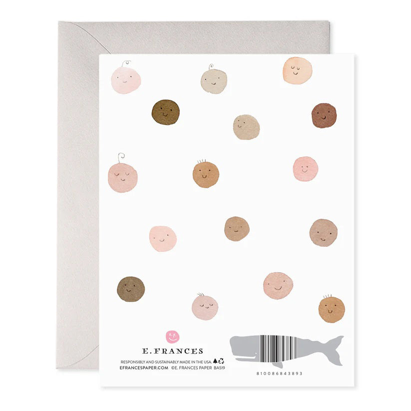 The E. FRANCES PAPER - WELCOME BABY GREETING CARD by E. FRANCES PAPER is a handcrafted watercolor card with "welcome baby!" in light blue, featuring smiling circular faces in diverse skin tones with little hair tufts, paired with a gray envelope, proudly made in the USA.
