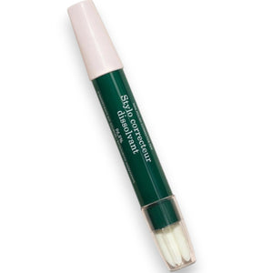 The MANUCURIST - CORRECTOR PEN by MANUCURIST INC lies diagonally on a white background. Reminiscent of a nail polish corrector pen, this green and pink pen labeled “Stylo correcteur dissimulant” features a pink cap and a clear bottom that reveals three white brush tips.