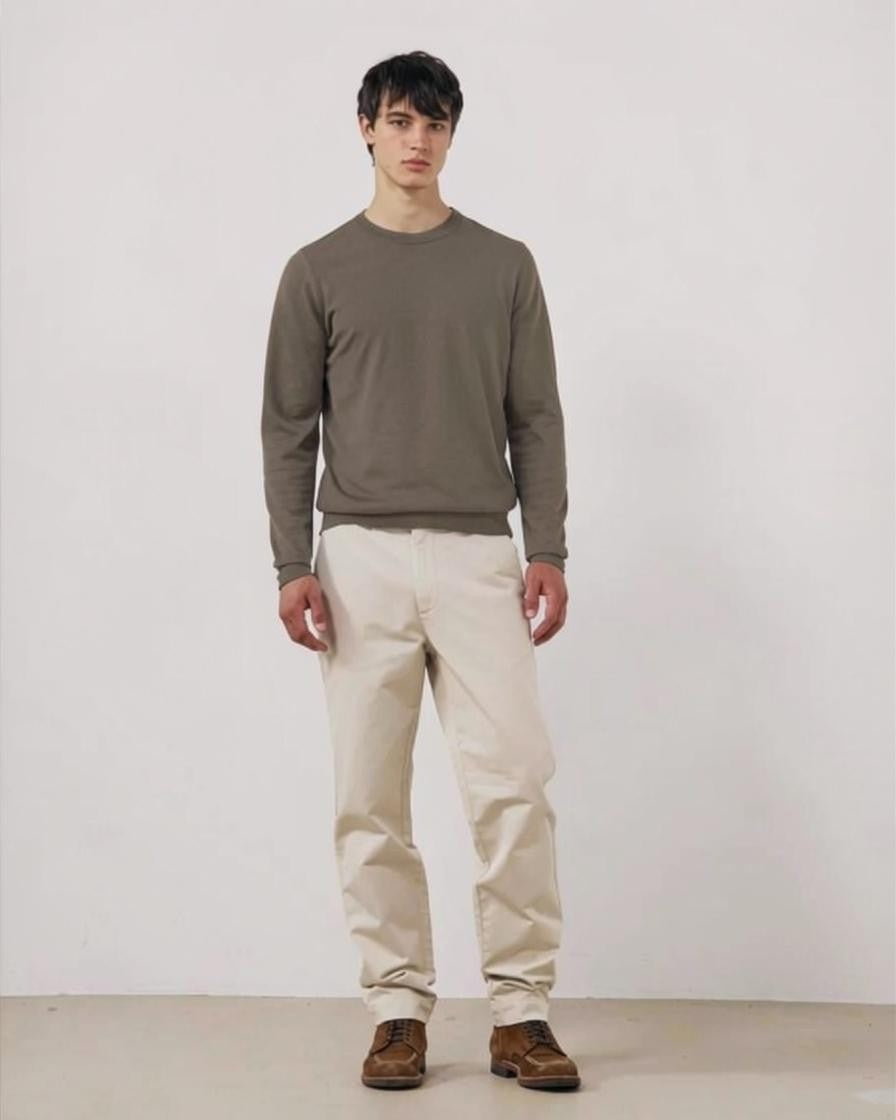 A person wearing the HARTFORD Extra-Fine Merino Wool Crew Pullover in Mushroom and beige pants stands with hands in pockets against a white background.