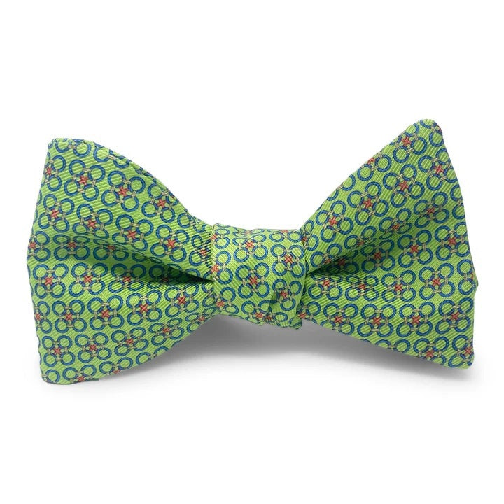 The PETER-BLAIR - CIRCLE CROSS SILK BOW TIE IN GREEN by BIRD DOG BAY features a green adjustable design adorned with a repeating pattern of blue and red rings, shown against a white background.
