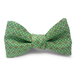 The PETER-BLAIR - CIRCLE CROSS SILK BOW TIE IN GREEN by BIRD DOG BAY features a green adjustable design adorned with a repeating pattern of blue and red rings, shown against a white background.