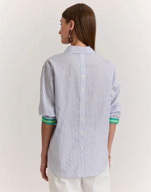 A woman with straight brown hair is shown from behind wearing the HINSON WU JULIANA Long Sleeve Shirt in Contrast Stripe, a 100% cotton blue and white vertical striped shirt with back buttons and green-trimmed sleeves, against a light background.