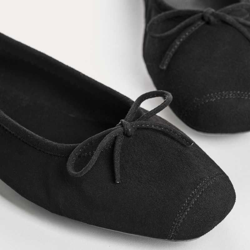 Wearing rolled-up blue jeans with REQINS - HARMONY SUEDE BALLERINA FLATS IN NOIR, featuring chic bow details—a timeless addition to any classic wardrobe.