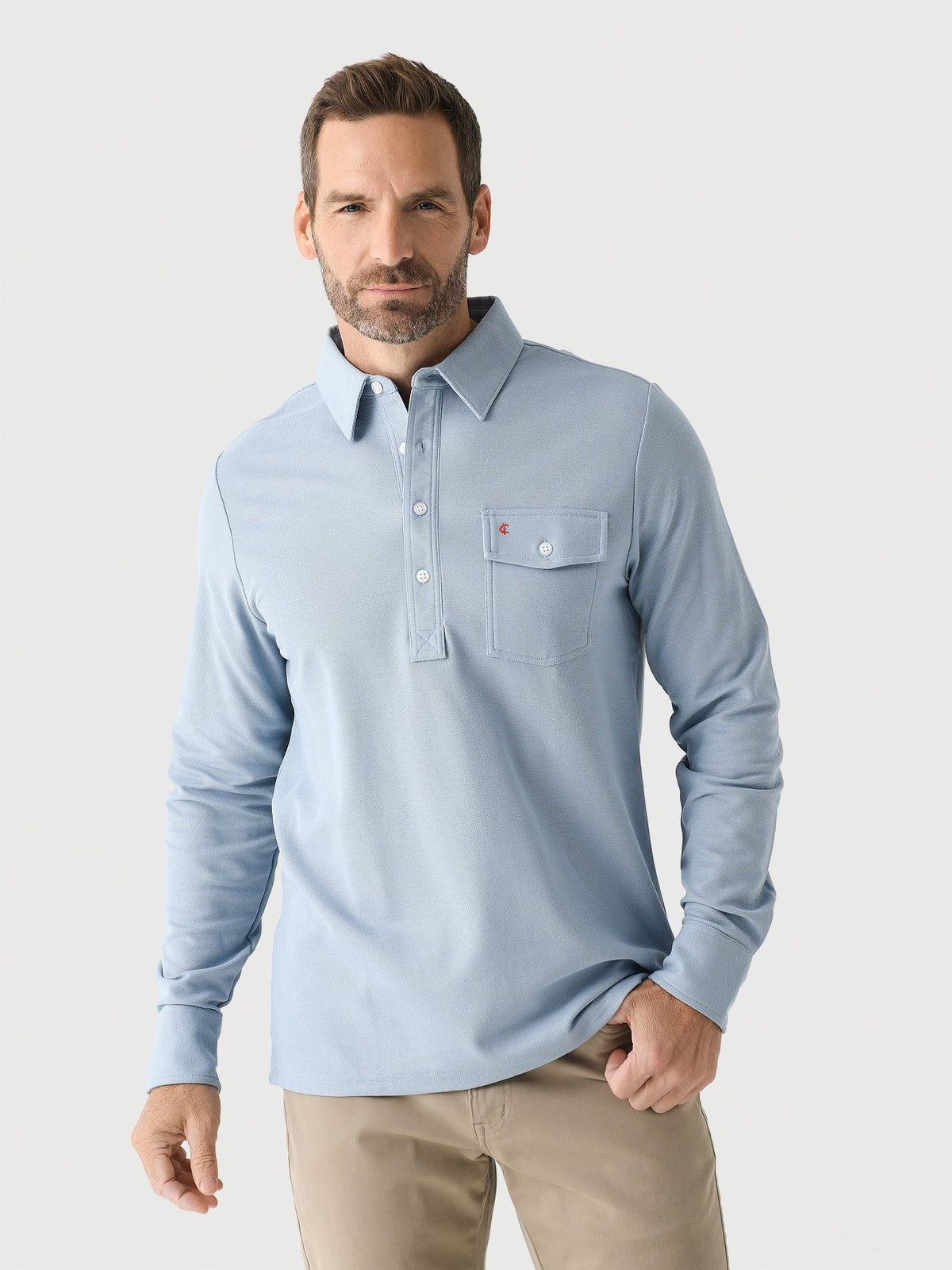A smiling man with short blond hair and a beard wears the CRIQUET Long Sleeve Players Polo Shirt in Mr Freeze, standing against a plain white background.