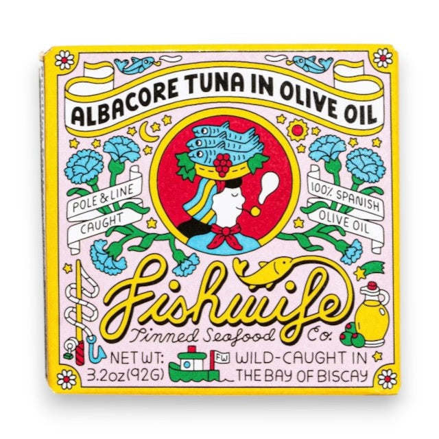 A vibrant tin of FISHWIFE Albacore Tuna in Olive Oil features a vintage-inspired design with a woman, flowers, lemons, and banners highlighting the product’s wild-caught and MSC-certified albacore tuna packed in Spanish olive oil.