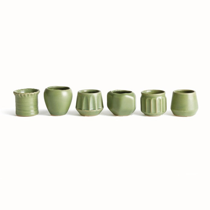 Six NAPA HOME AND GARDEN - DEZIE MINI POTS by NAPA HOME AND GARDEN, each uniquely shaped and textured in green, are crafted from high-fired stoneware and arranged in a row on a white background.