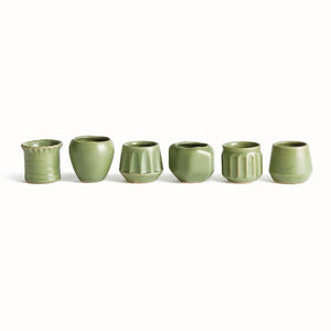 Six NAPA HOME AND GARDEN - DEZIE MINI POTS by NAPA HOME AND GARDEN, each uniquely shaped and textured in green, are crafted from high-fired stoneware and arranged in a row on a white background.
