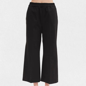 A person is wearing black, pull-on straight-leg cropped pants from MEIMEIJ with an elastic waistband. The bottom part of their legs and feet are visible, highlighting the sleek seam detail, but the top part of the body is not shown. The background is plain white.