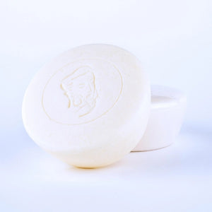 Two round, white BAUDELAIRE - M.B. SHAVING SOAP bars by BAUDELAIRE are displayed. The front bar features an embossed profile of a bearded man, set against a plain white background that evokes the clean, minimalist feel and hints at the smooth razor glide and nourishing shea butter found in each bar.