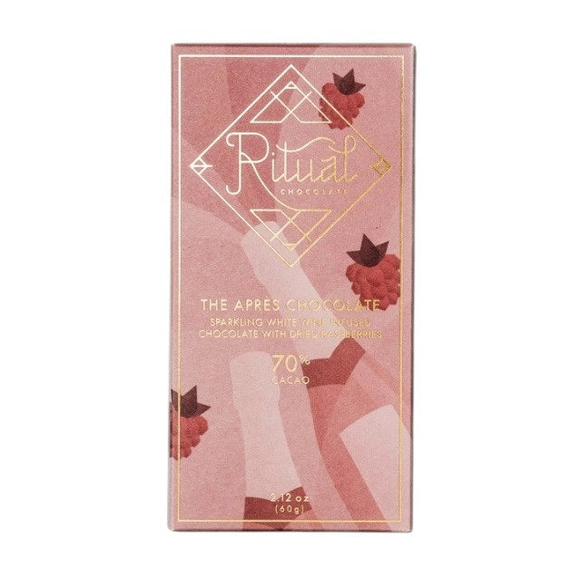 A rectangular chocolate bar with a pinkish wrapper adorned with minimalist illustrations of raspberries and abstract shapes. The packaging reads "RITUAL CHOCOLATE - THE APRES CHOCOLATE BAR 70%, Sparkling Wine Infused Chocolate with Dried Raspberries," 2.12 oz (60g).