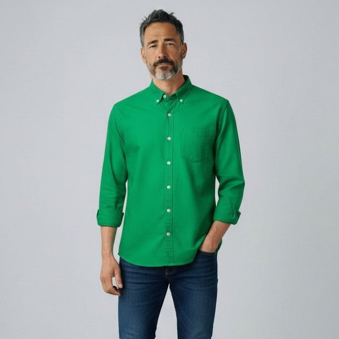 A man with short gray hair and a beard stands facing forward, wearing the FRANK &amp; EILEEN LUKE Men's Button Up Shirt in Famous Denim Birdie with rolled-up sleeves and dark blue jeans against a plain light gray background.