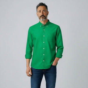 A man with short gray hair and a beard stands facing forward, wearing the FRANK & EILEEN LUKE Men's Button Up Shirt in Famous Denim Birdie with rolled-up sleeves and dark blue jeans against a plain light gray background.