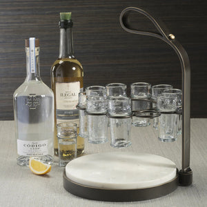 The ZODAX TEQUILERO 10 Shot Tequila Set features a circular white marble cutting board with an iron handle and metal frame, holding ten empty shot glasses arranged in a ring.