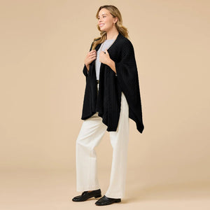 A woman wearing a black SOFTIES - SOLID RIB MARSHMALLOW SHAWL over a grey top and white trousers.
