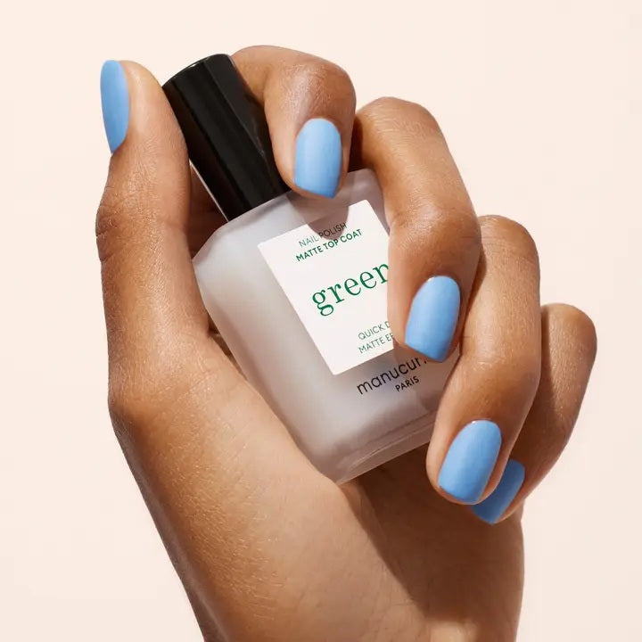 A frosted glass bottle of MANUCURIST INC’s GREEN™ NAIL POLISH MATTE TOP COAT, a plant-based nail polish, featuring a black cap and a white label.