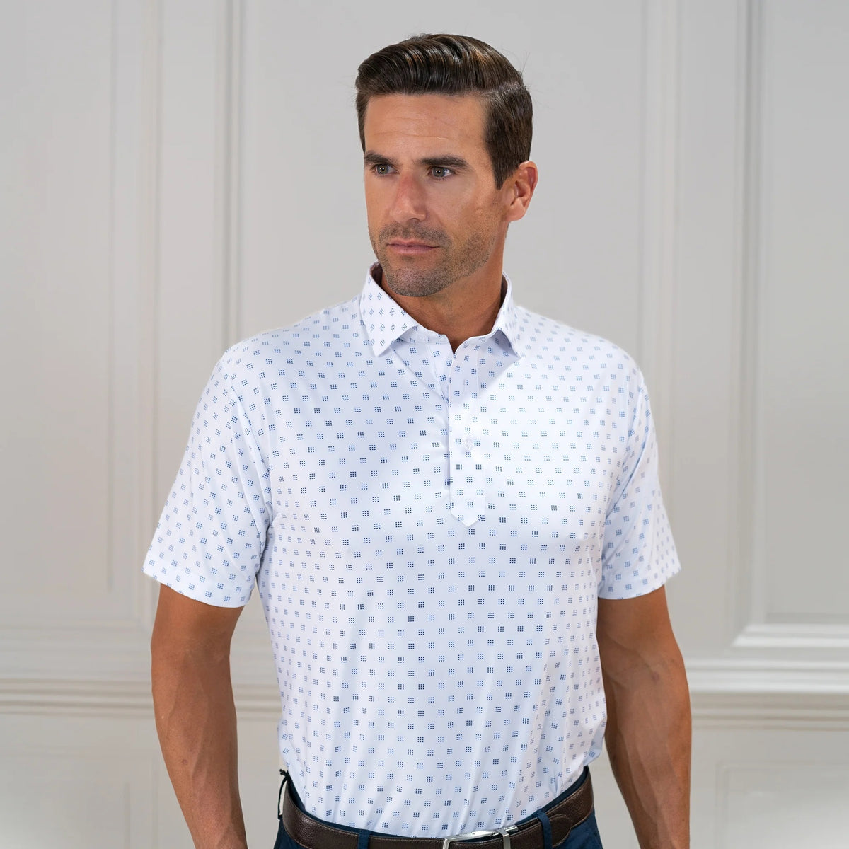 The COLLARS AND CO FEATHERWEIGHT FLEX POLO IN ORACLE WHITE features white fabric with a repeating pattern of small blue 3x3 dot squares. Slightly creased at the center, its 6-way stretch design ensures all-day comfort.
