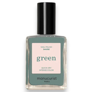 A hand with short, oval-shaped nails painted in MANUCURIST INC’s sophisticated GREEN™ Nail Polish in Sage—a chic gray vegan shade—is held in front of bright pink-red flower petals.