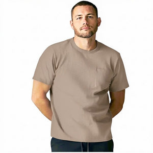 A man with short curly hair and a beard wears the MACK WELDON Heavyweight Slub Cotton Pocket T-Shirt in Desert Taupe and dark pants, standing against a plain white background.
